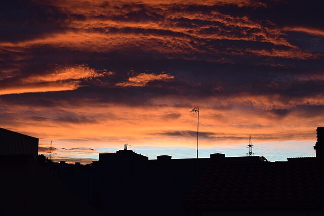 Silhouetted buildings beneath a cloudy sunset in urban Barcelona.